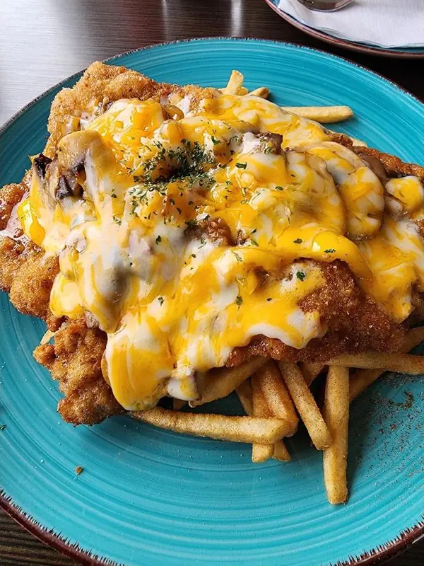 Gypsy schnitzel under melted cheese and mushrooms over fries