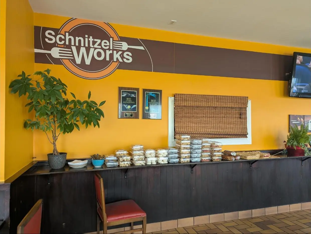 The dining room: marigold walls, the Schnitzel Works logo on a brown band, red chairs and a pastry counter