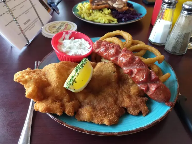 Breaded schnitzel with lemon, a smoked sausage, onion rings and tartar sauce