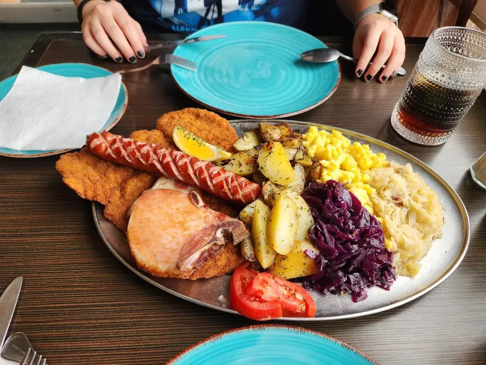 Platter for Two piled with schnitzel, a smoked pork chop, sausage, roasted potatoes, spätzle, red cabbage and speck kraut