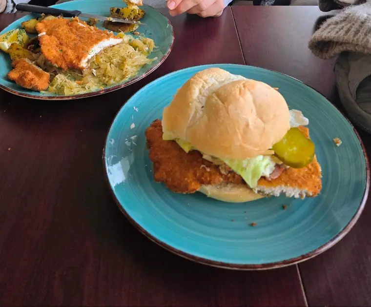 Schnitzel sandwich on a Kaiser bun with lettuce and pickle on a turquoise plate